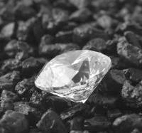 Ein glasklarer Diamant liegt auf schwarzem Geröll.