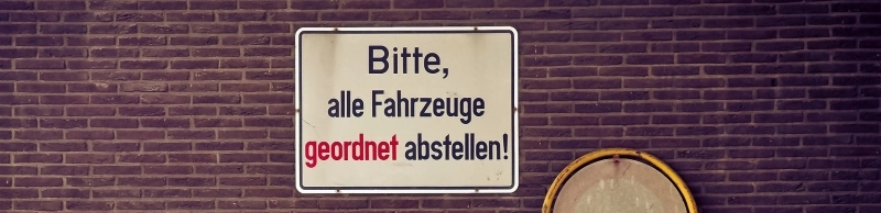 Auf einem alten Schild steht: Bitte, alle Fahrzeuge geordnet abstellen!