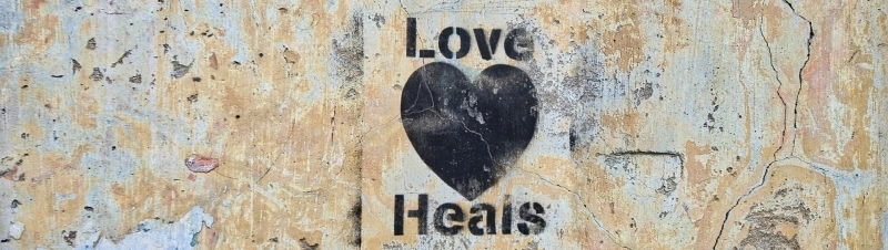Schwarzes Herz auf bröckelnder Wand mit Schriftzug Love Heals – Symbol für die Heilung seelischer Verletzungen.