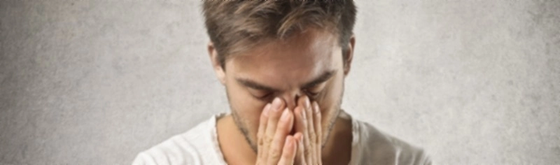 Ein erschöpfter Mann hält sich verzweifelt die Hände vors Gesicht. Das Bild verdeutlicht die belastenden Begleiterscheinungen von Einsamkeit wie Schlafstörungen und seelischen Schmerz.
