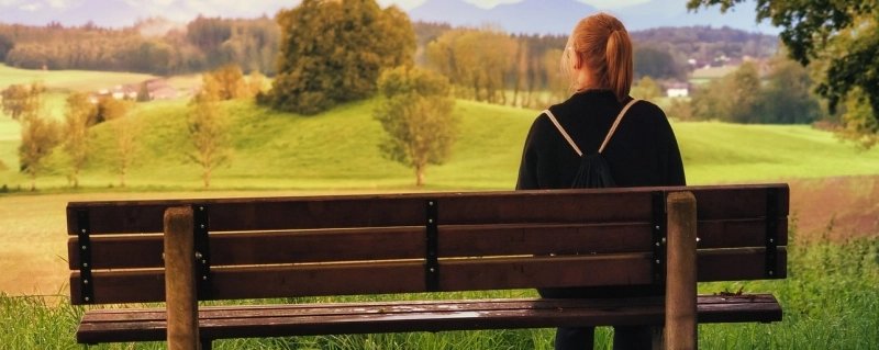 Eine Frau sitzt allein auf einer Parkbank und blickt in eine weite Landschaft – Symbol für die Ruhe nach der Trennung und den Beginn der Selbstliebe.