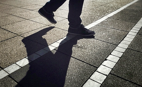 Ein Mensch geht mit seinem Schatten über einen Weg und macht sichtbar, dass Licht und Schatten untrennbar zusammengehören.