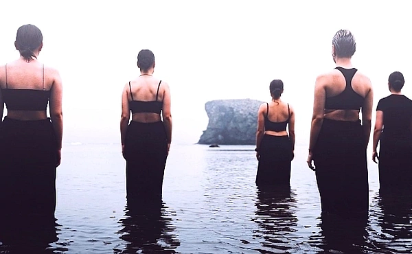 Mehrere Menschen stehen schweigend im Wasser und blicken auf einen Felsen – Sinnbild für die spirituelle Auseinandersetzung mit Krebs und den inneren Weg in der Reinkarnationstherapie.