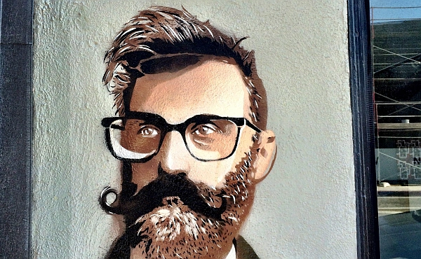 Urbanes Wandbild eines Mannes mit markantem Stil (Bart, Brille, Fliege). Das Bild symbolisiert Individualität und den Mut, sich von der Masse abzuheben.