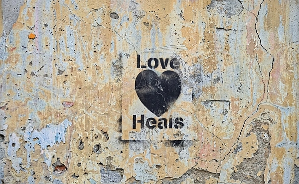 Schwarzes Herz auf bröckelnder Wand mit Schriftzug Love Heals – Symbol für die Heilung seelischer Verletzungen.